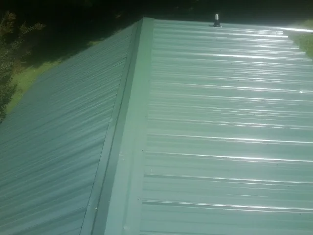 New green metal panels meeting at the ridge of a roof — Flat Roof Repair work by our crew in West Valley City