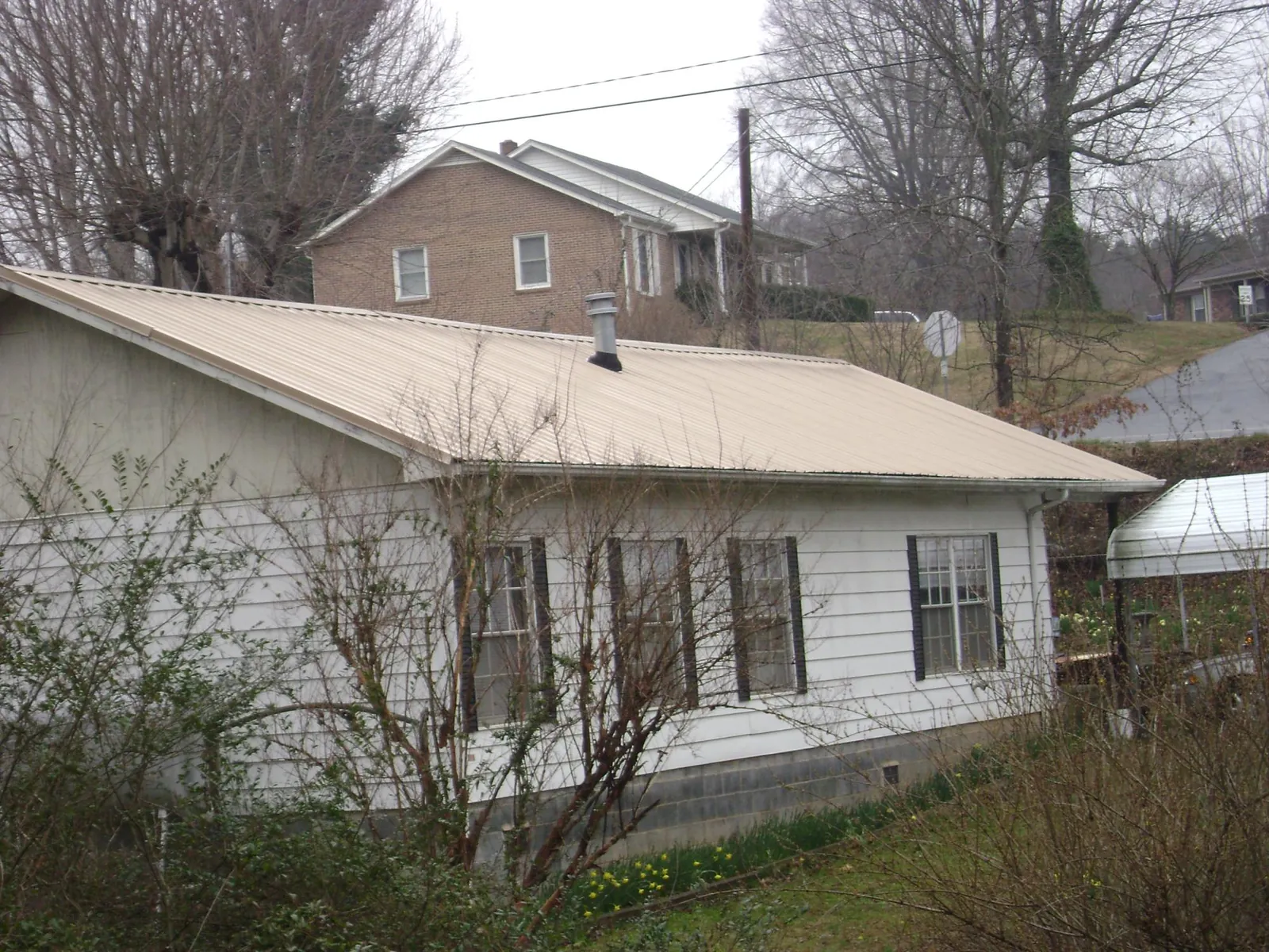 Tan metal roof on a white sided house set into a hillside — Commercial Roofing by Roofing Brothers in West Valley City